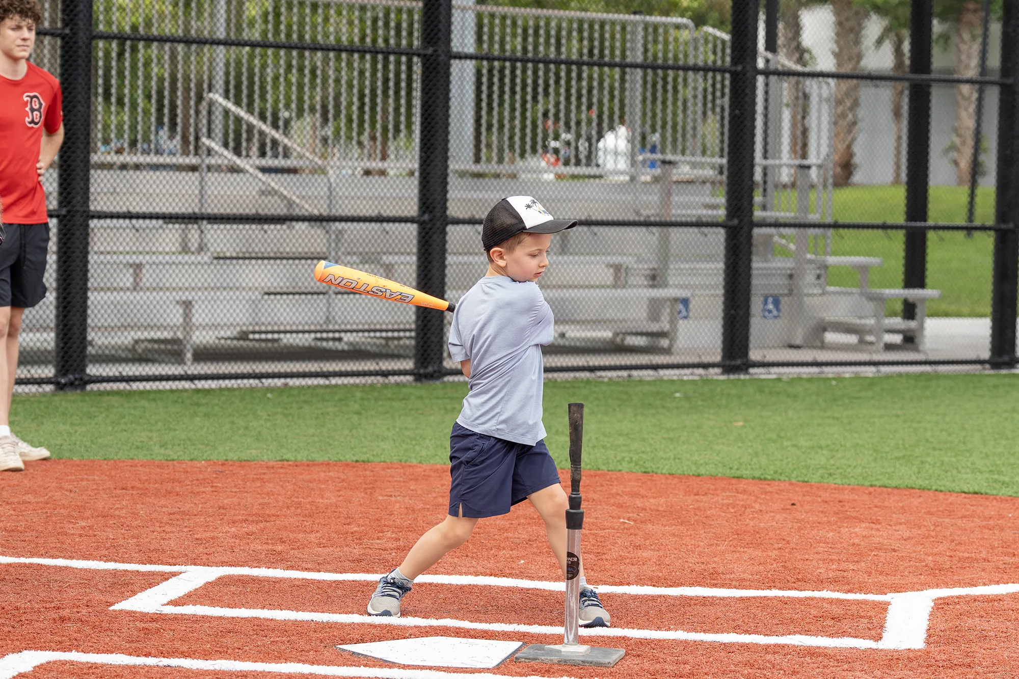 Young baseball player batting from a tee on a 2026 festival baseball diamond